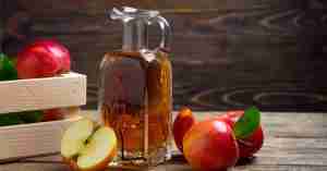 An image of pitcher filled with cider beside cut apples