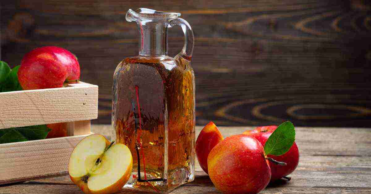 An image of pitcher filled with cider beside cut apples