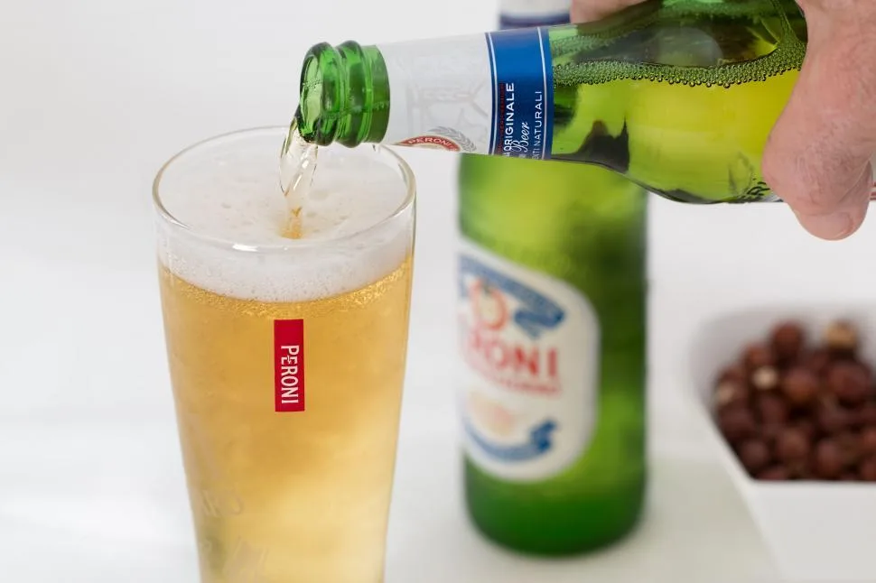 An image of a person's hand pouring a Peroni Nastro Azzurro into a glass