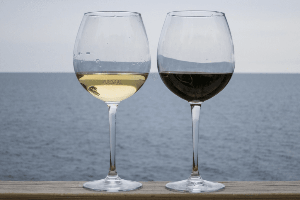 Red and white wine next to each other on a table with the sea in the background