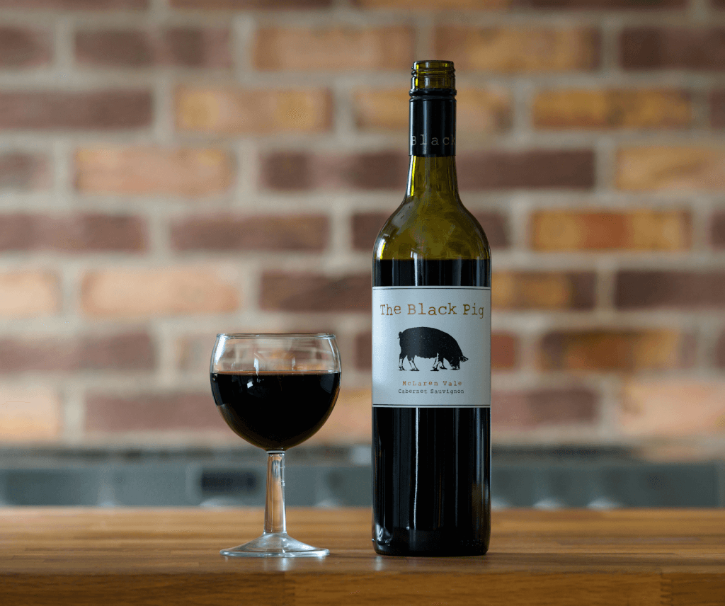 The Black Pig red wine on a table with a glass next to it