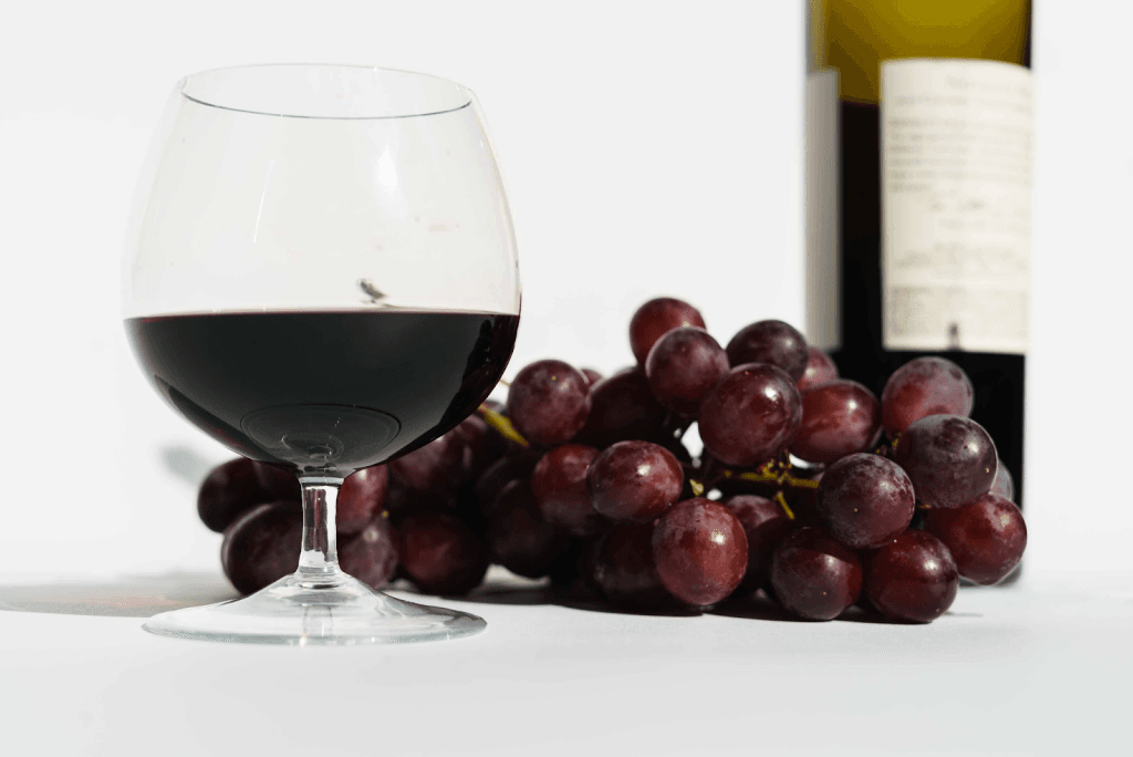 A image of a wine glass with vermouth and a bunch of grapes beside it