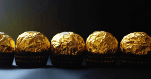 Is Ferrero Rocher Gluten-Free? An image of five wrapped Ferrero Rocher Chocolates set on a dark background