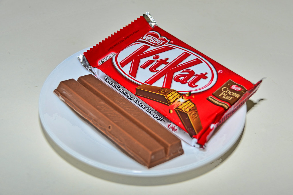 An image of wrapped KitKat with two KitKat pieces on a ceramic plate